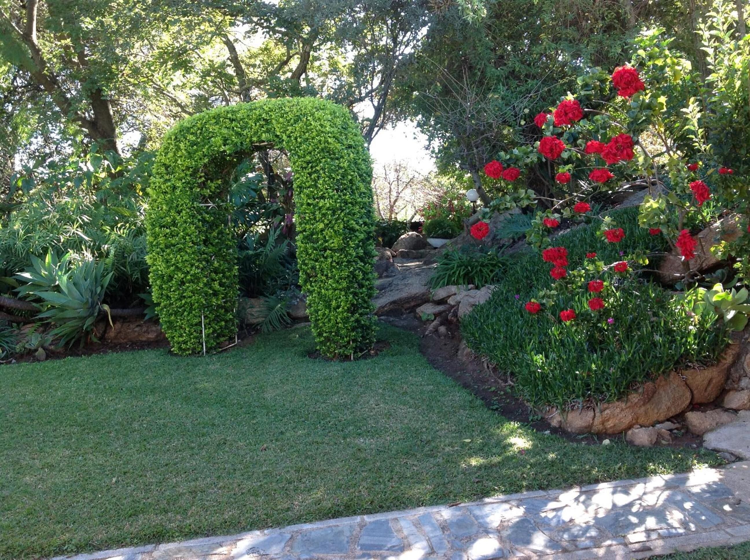 Un jardín con un arco verde, flores rojas y un sendero de piedra.