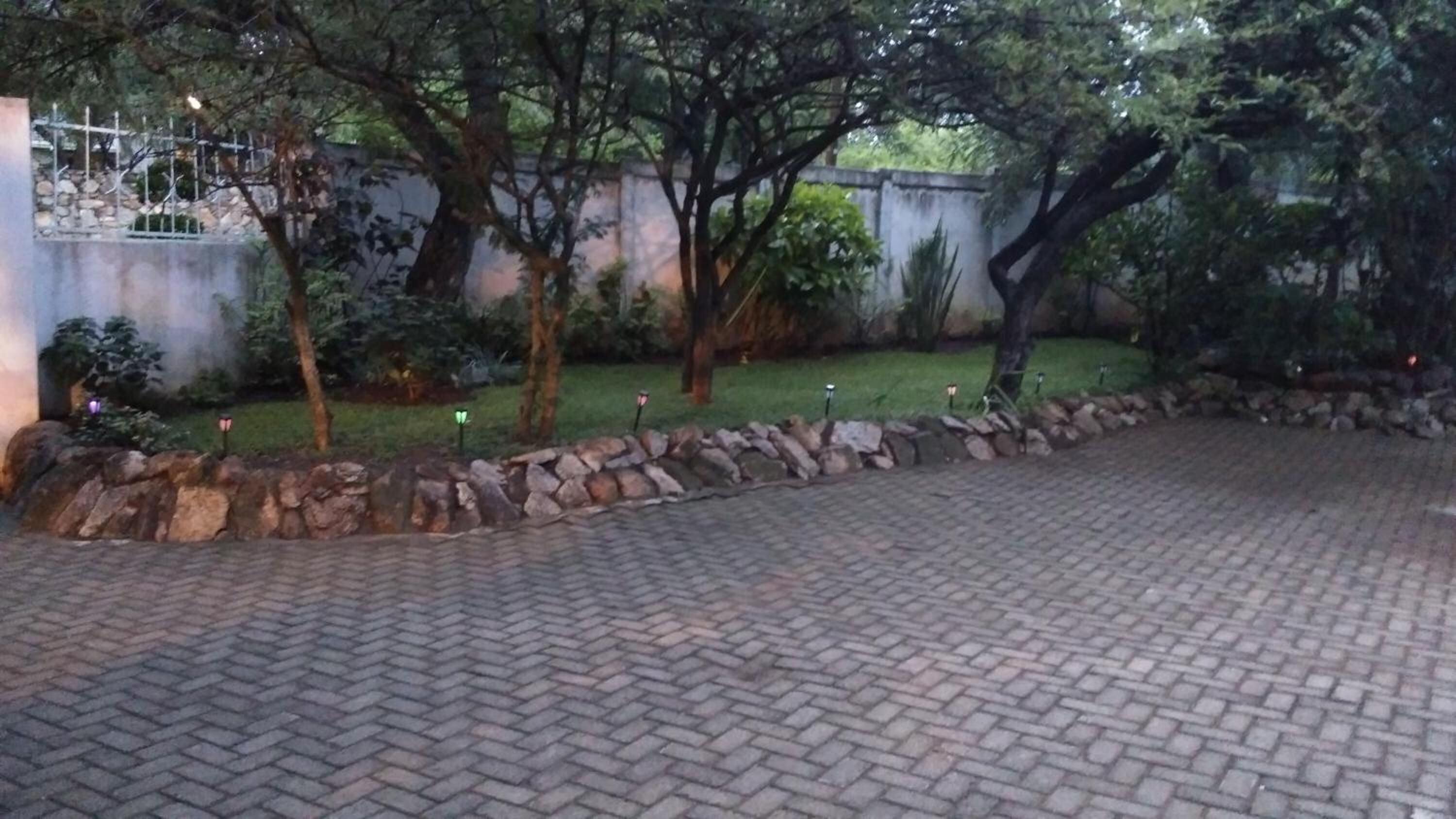 A paved driveway leading to a stone wall, surrounded by trees and a grassy area.