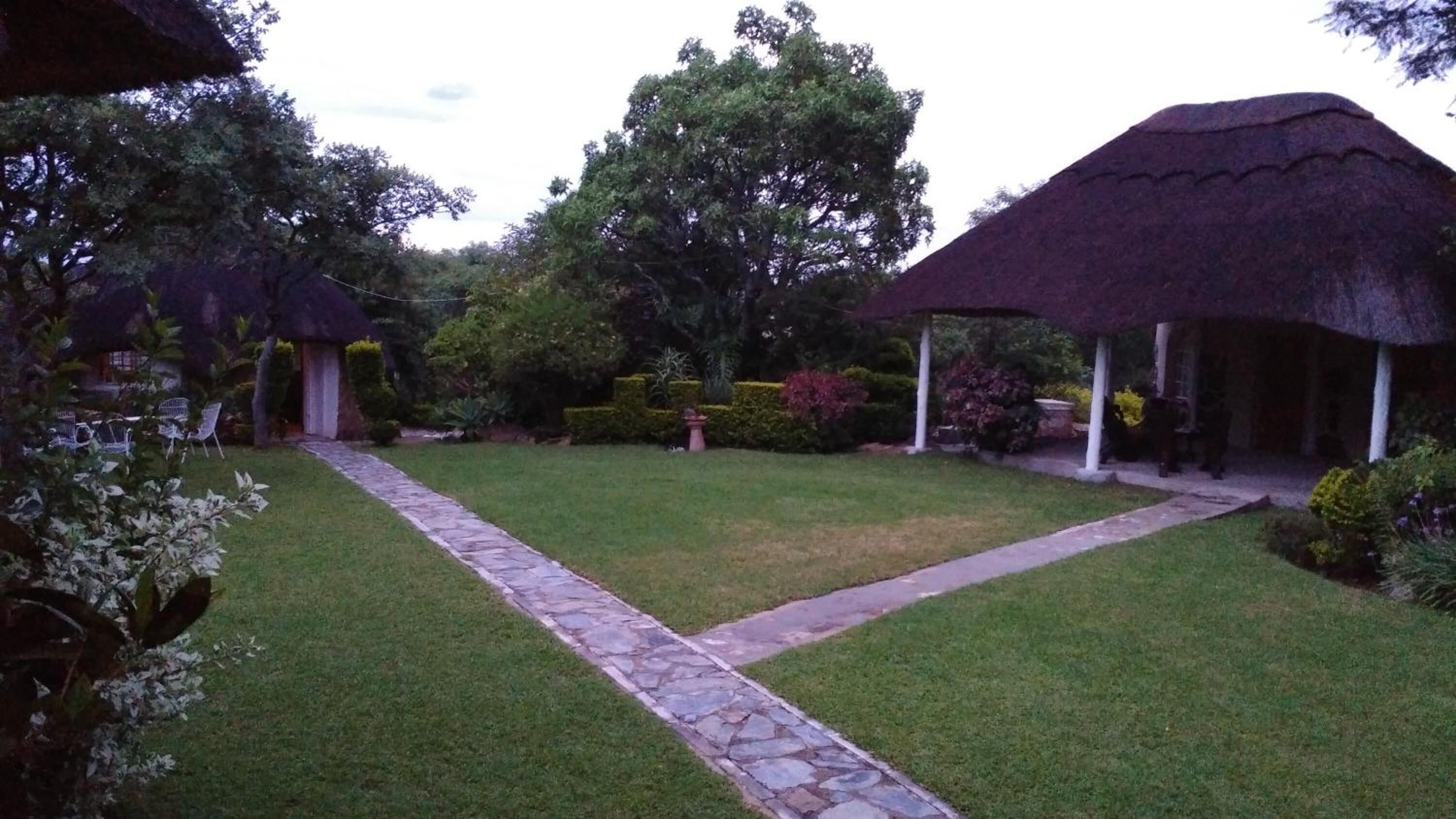 Un giardino con edifici a tetto di paglia, un sentiero in pietra e diverse piante.
