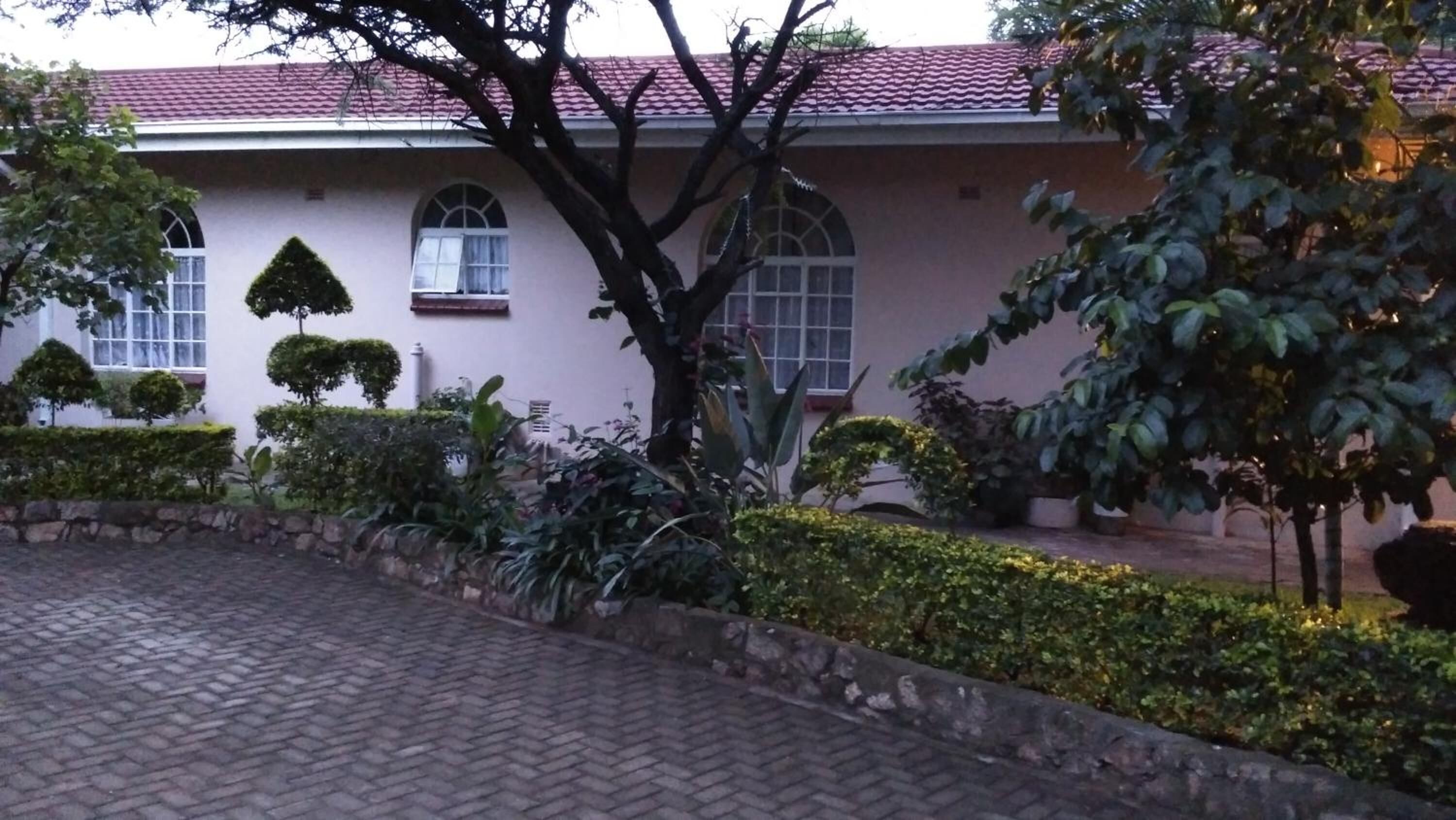 A building with a red-tiled roof, arched windows, and a paved courtyard with hedges and potted plants.