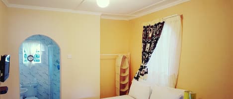 Un dormitorio con cama, mesita de noche, lámpara, ventana con cortinas, zona de ducha y baño con inodoro y lavabo.