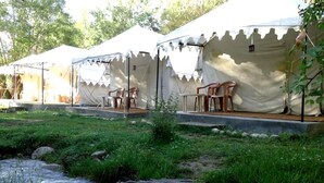 A row of tents with outdoor seating and a stream in the foreground. - TIH Royal Desert Camp (Leh)