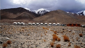 A row of white tents in a rocky, mountainous area with snow-capped peaks in the background. - TIH Ladakh Summer Camp Pangong (Leh)