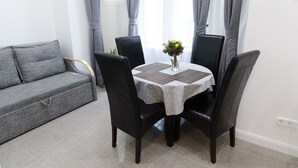 Un coin repas avec une table dressée pour quatre personnes, entourée de chaises noires, d’un canapé gris et d’un vase avec des fleurs posé sur la table.