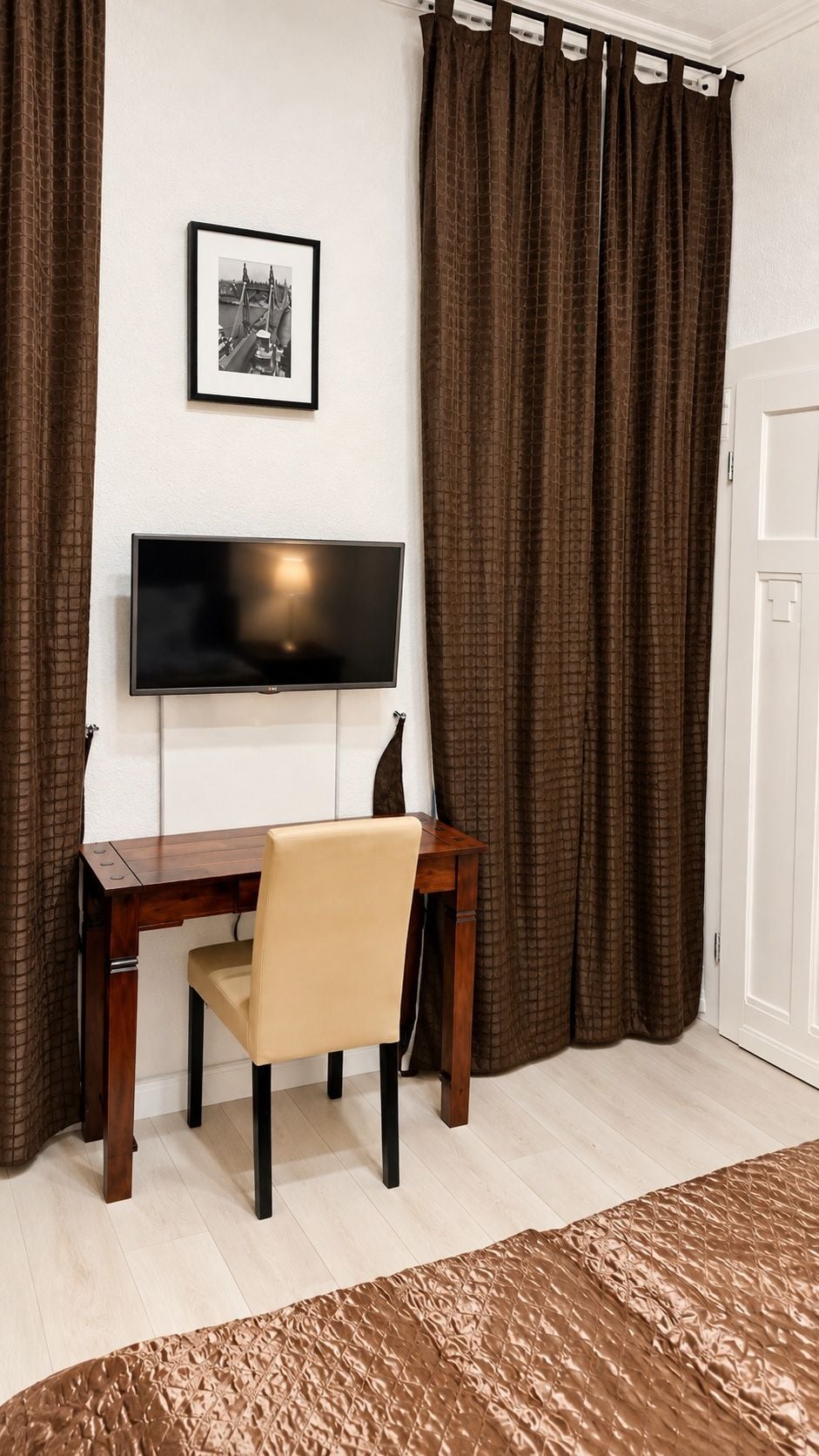 A room with a desk, chair, television, and curtains.