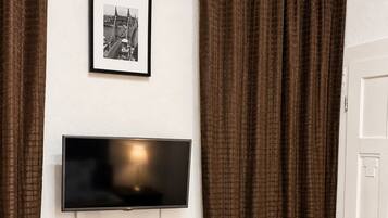 A room with a desk, chair, television, and curtains.