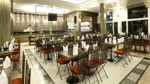 A spacious dining area with multiple tables and chairs, a modern kitchen in the background, and a large window providing natural light. - Royal Hills Golf Resort and Spa (Nakhon Nayok)