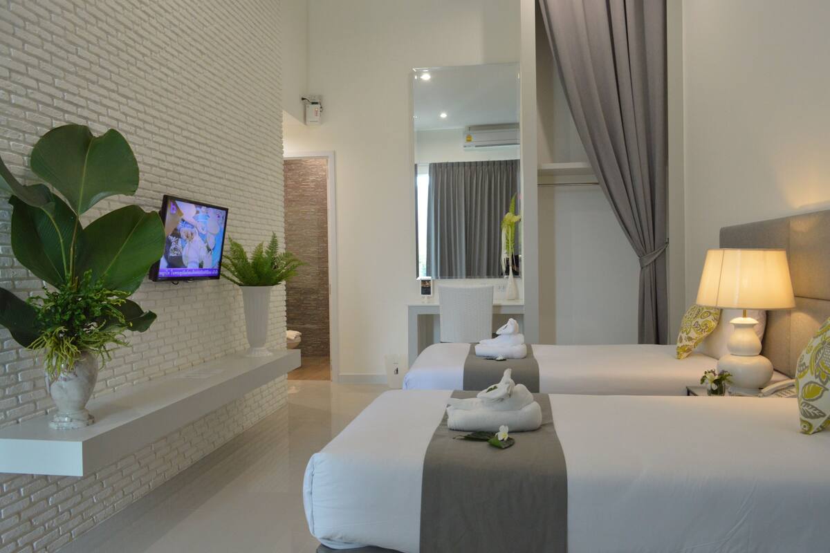 A hotel room with two beds, a TV, a mirror, a lamp, and a potted plant.