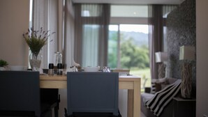 A dining area with a table set for two, a vase with flowers, salt and pepper shakers, and a view of the outdoors through large windows. - Royal Hills Golf Resort and Spa (Nakhon Nayok)