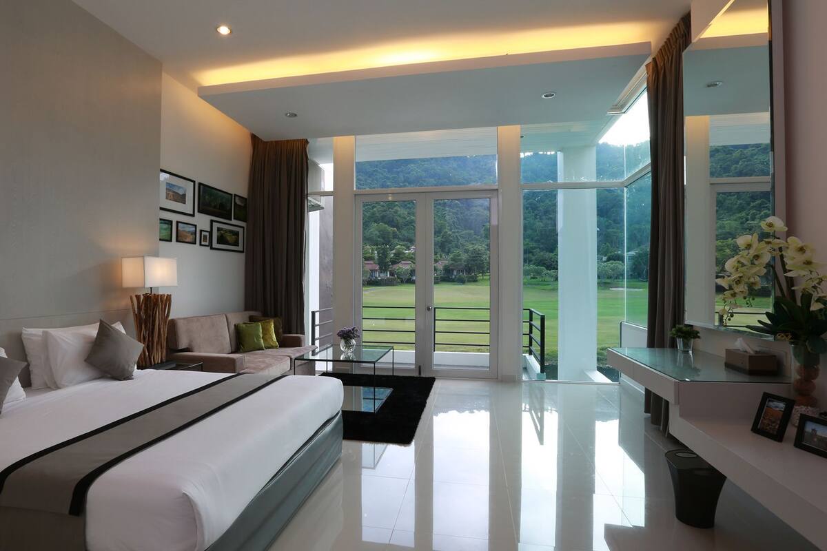 A modern hotel room with a large bed, a seating area, and a balcony with a view of the countryside.