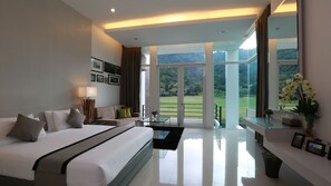 A modern hotel room with a large bed, a seating area, and a balcony with a view of the countryside.