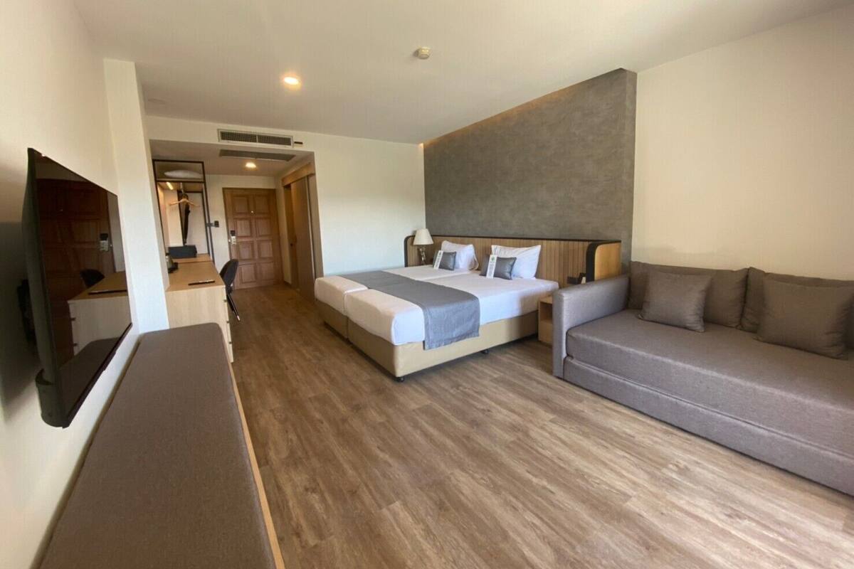 A hotel room with a bed, a sofa, a desk, and a TV.