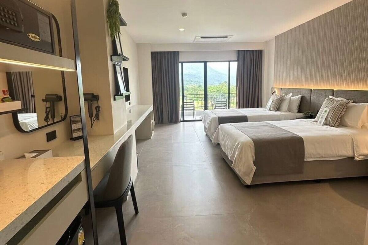 A hotel room with a desk, two beds, a large window with a view, and a balcony.
