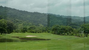 Un campo de golf con un estanque, búnkeres de arena y una colina boscosa al fondo.