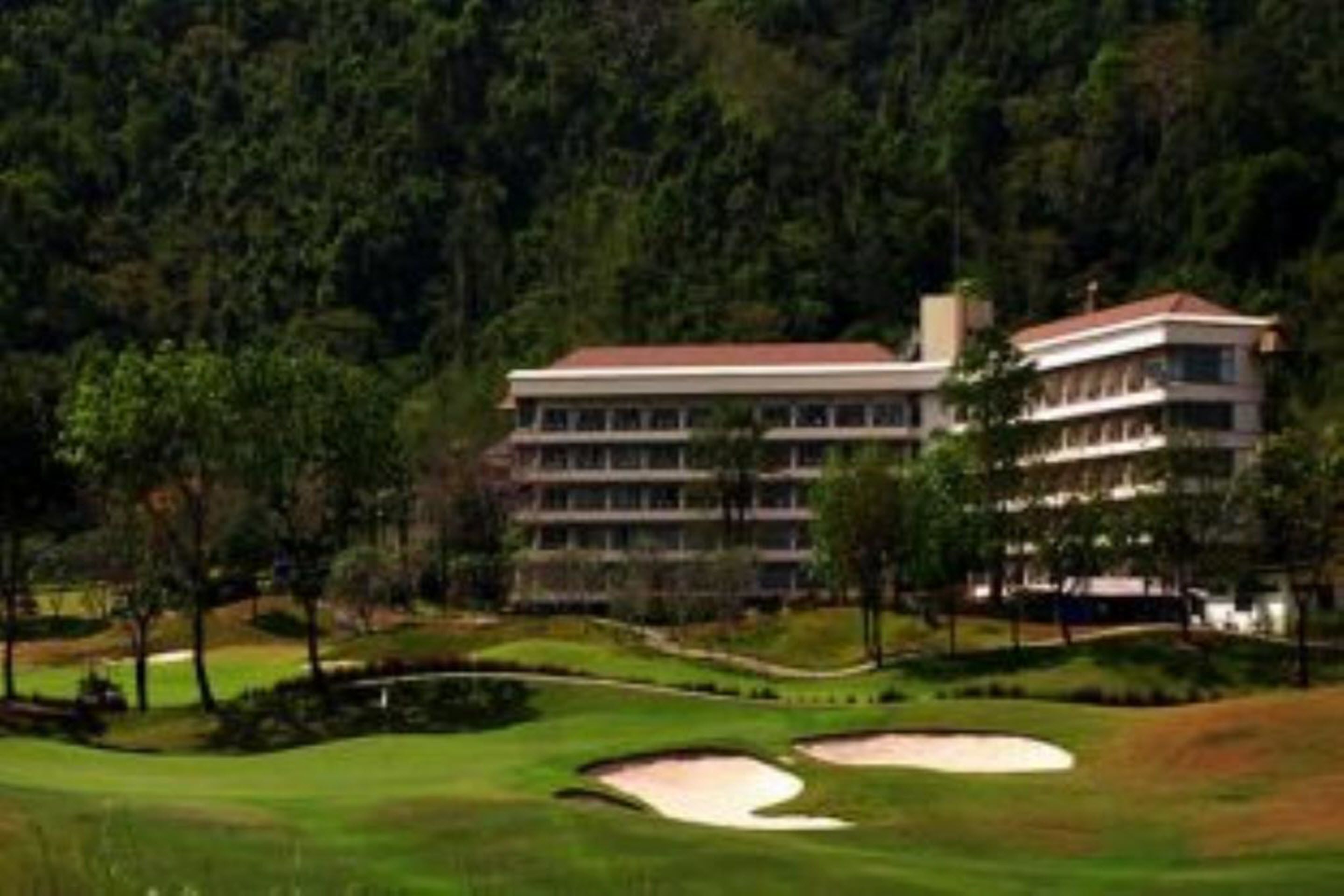 A large, multi-story building with a flat roof, surrounded by a well-maintained golf course with sand bunkers and trees.