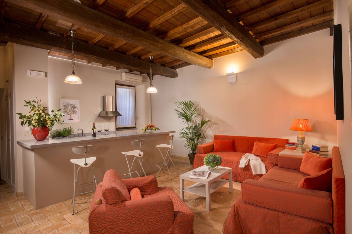 A cozy living area with a kitchen, featuring a wooden ceiling, a red sofa set, a coffee table, and a bar with stools.