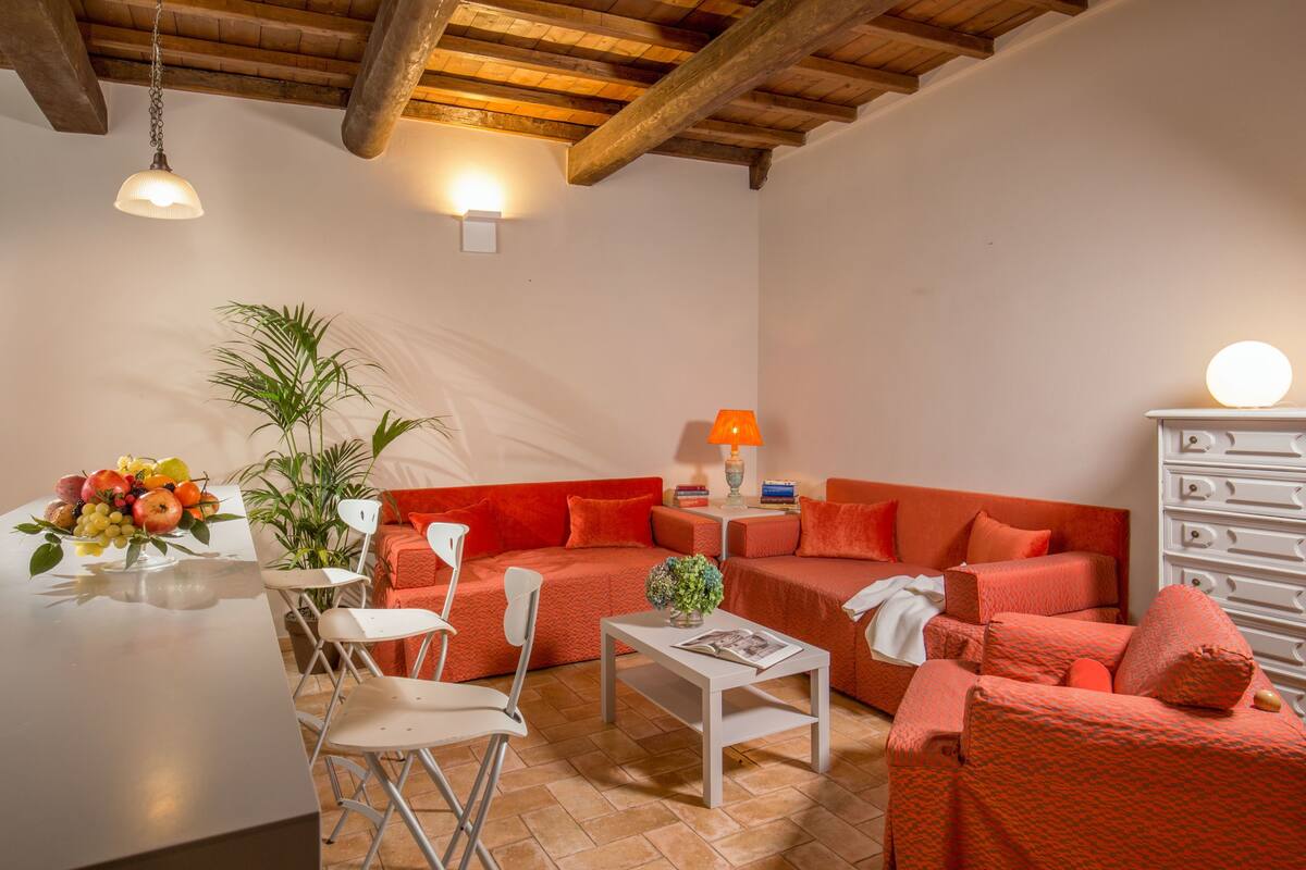 A living room with a wooden ceiling, a sofa set, a dining table with chairs, a lamp, and a plant.