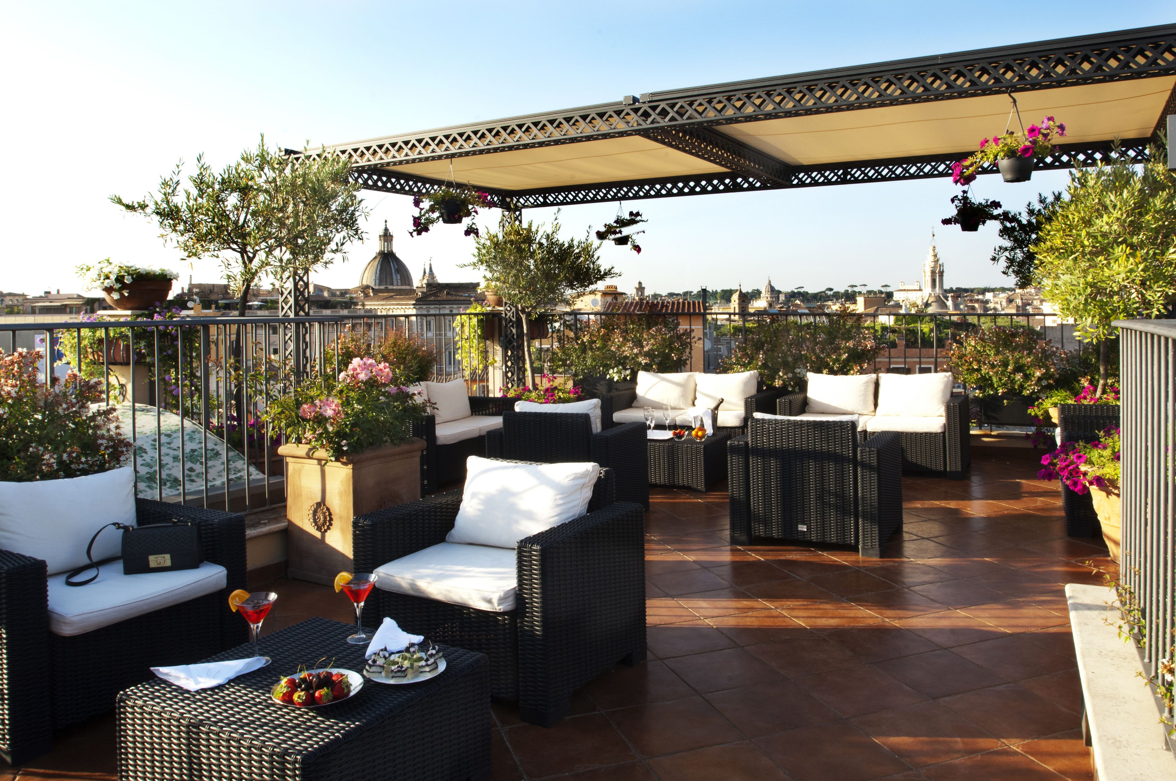 A rooftop terrace with wicker furniture, potted plants, and a view of the cityscape.
