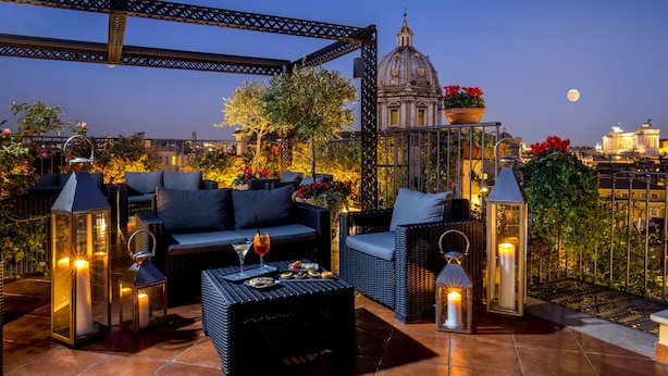 A rooftop terrace with wicker furniture, candles, and potted plants. - Boutique Hotel Campo dé Fiori (Rome)