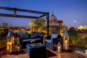 A rooftop terrace with wicker furniture, candles, and potted plants. - Boutique Hotel Campo dé Fiori (Rome)