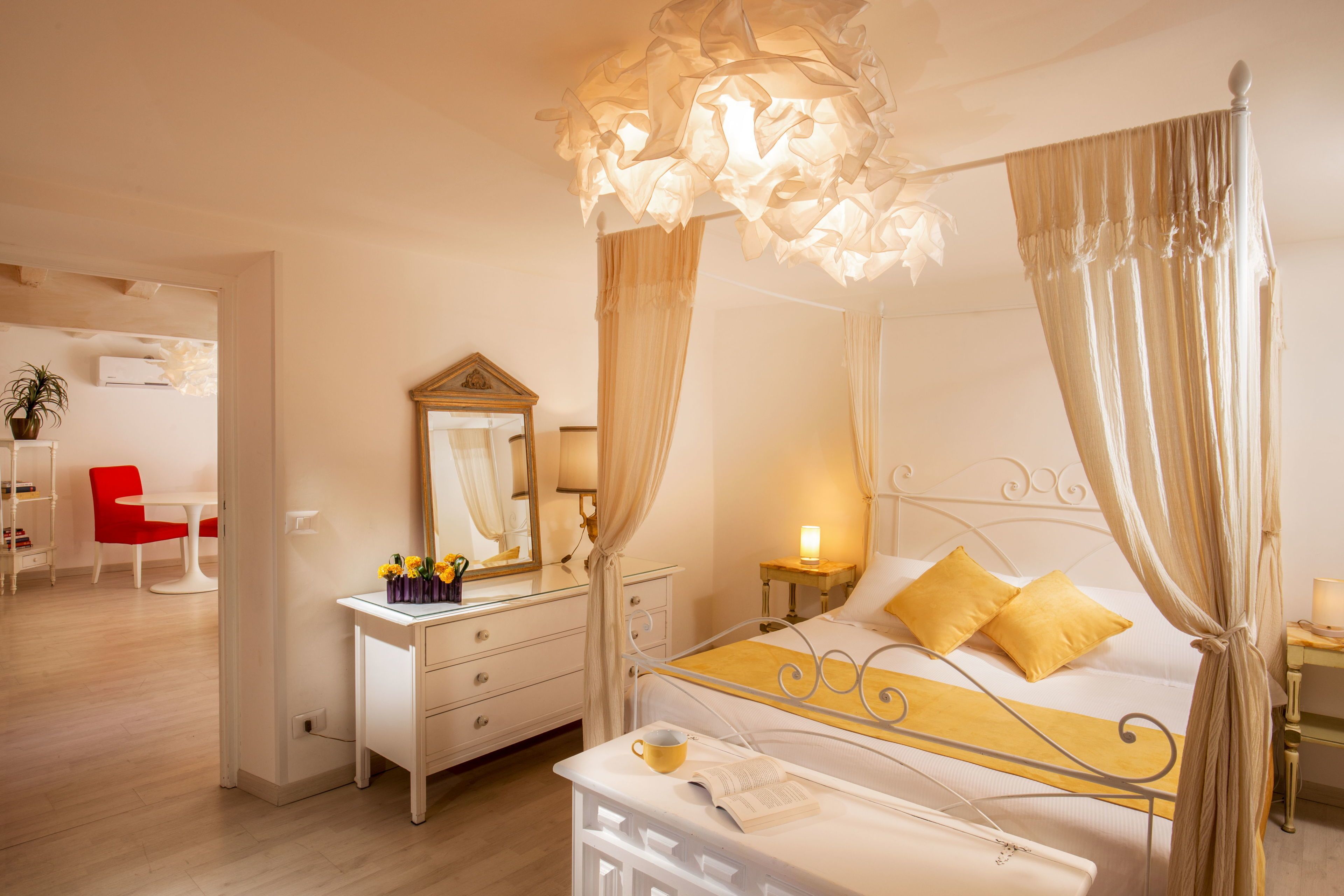 Un lit à baldaquin, une table de chevet avec une lampe et une chaise rouge dans une chambre d’hôtel.