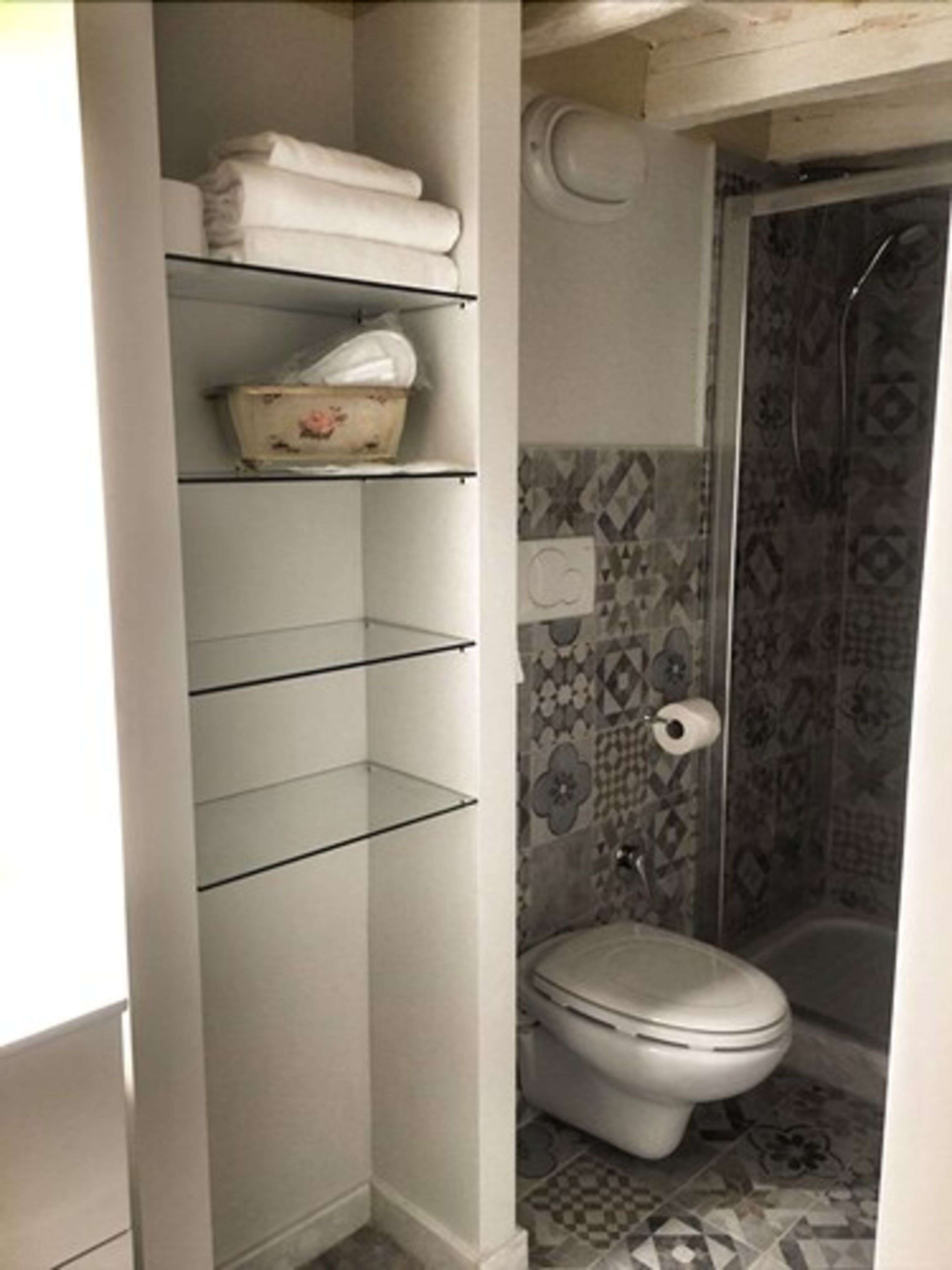 Un bagno con il WC, una doccia e uno scaffale con articoli da toilette.