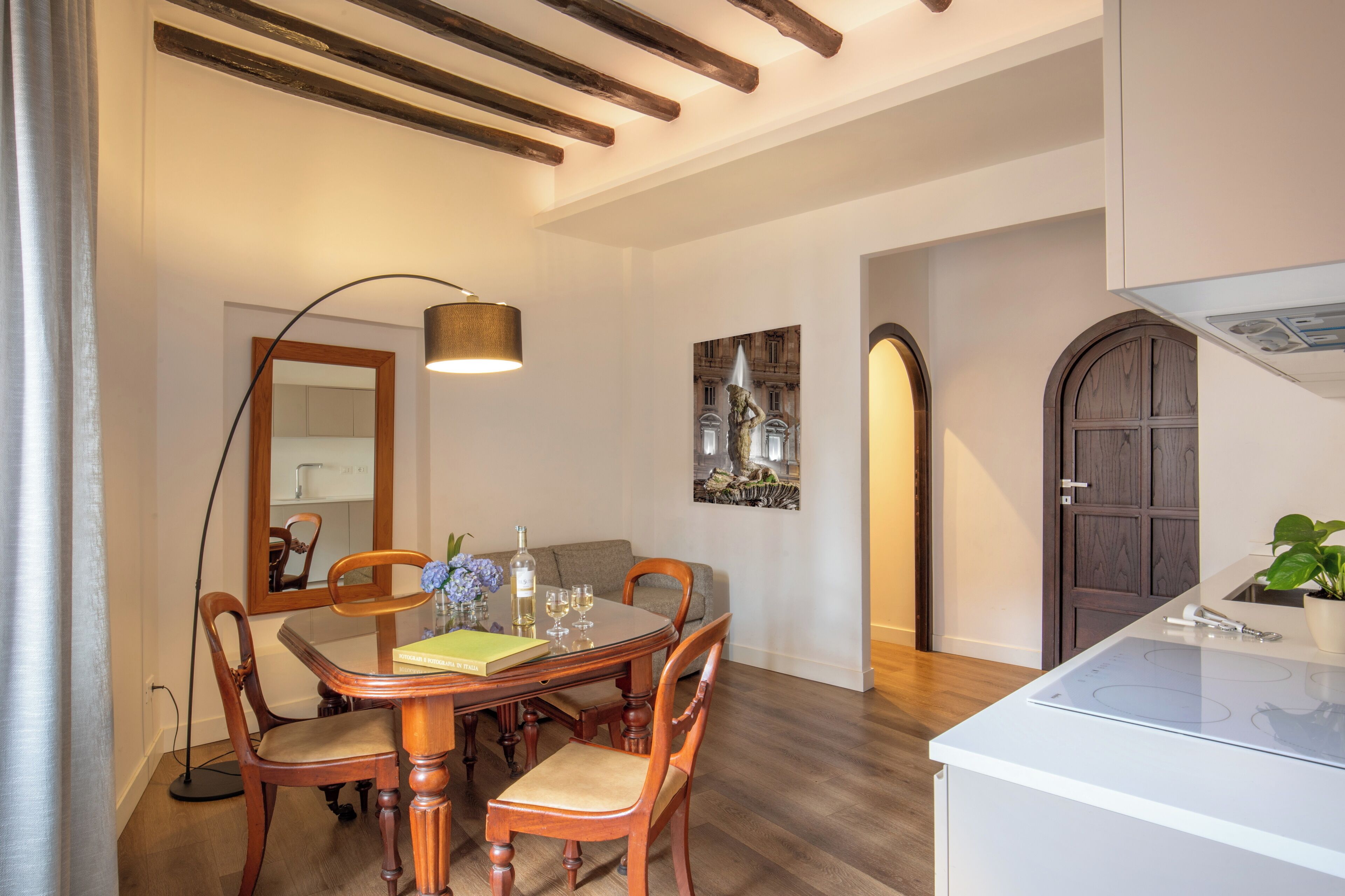 Un comedor con una mesa de madera, sillas y una lámpara. Hay una zona de cocina con estufa y una planta en maceta.
