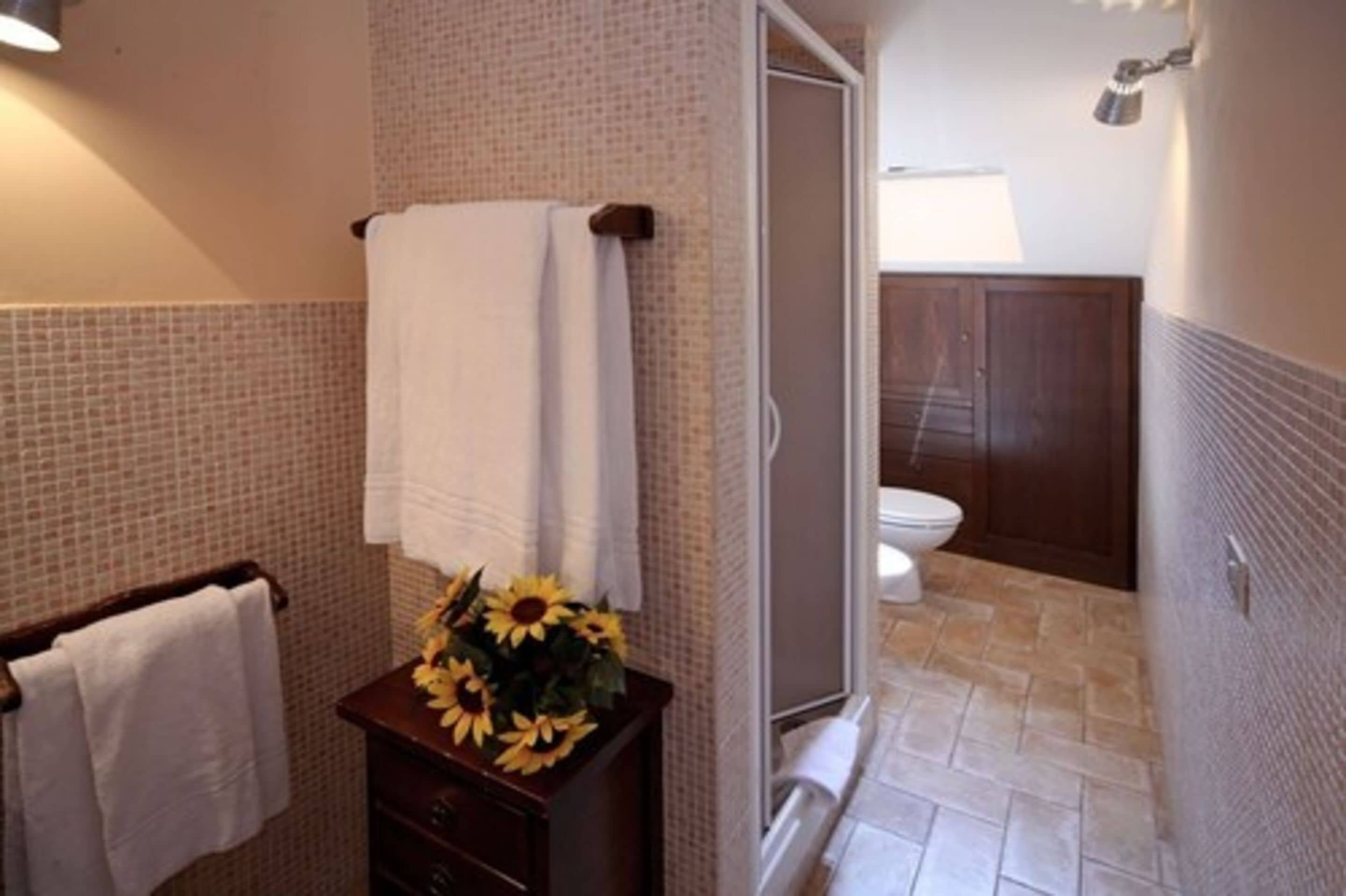Une salle de bain avec une douche, des toilettes et un lavabo agrémenté d’un vase de tournesols.