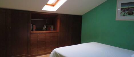 A bedroom with a skylight, a bed, a wooden wardrobe, and a green wall.