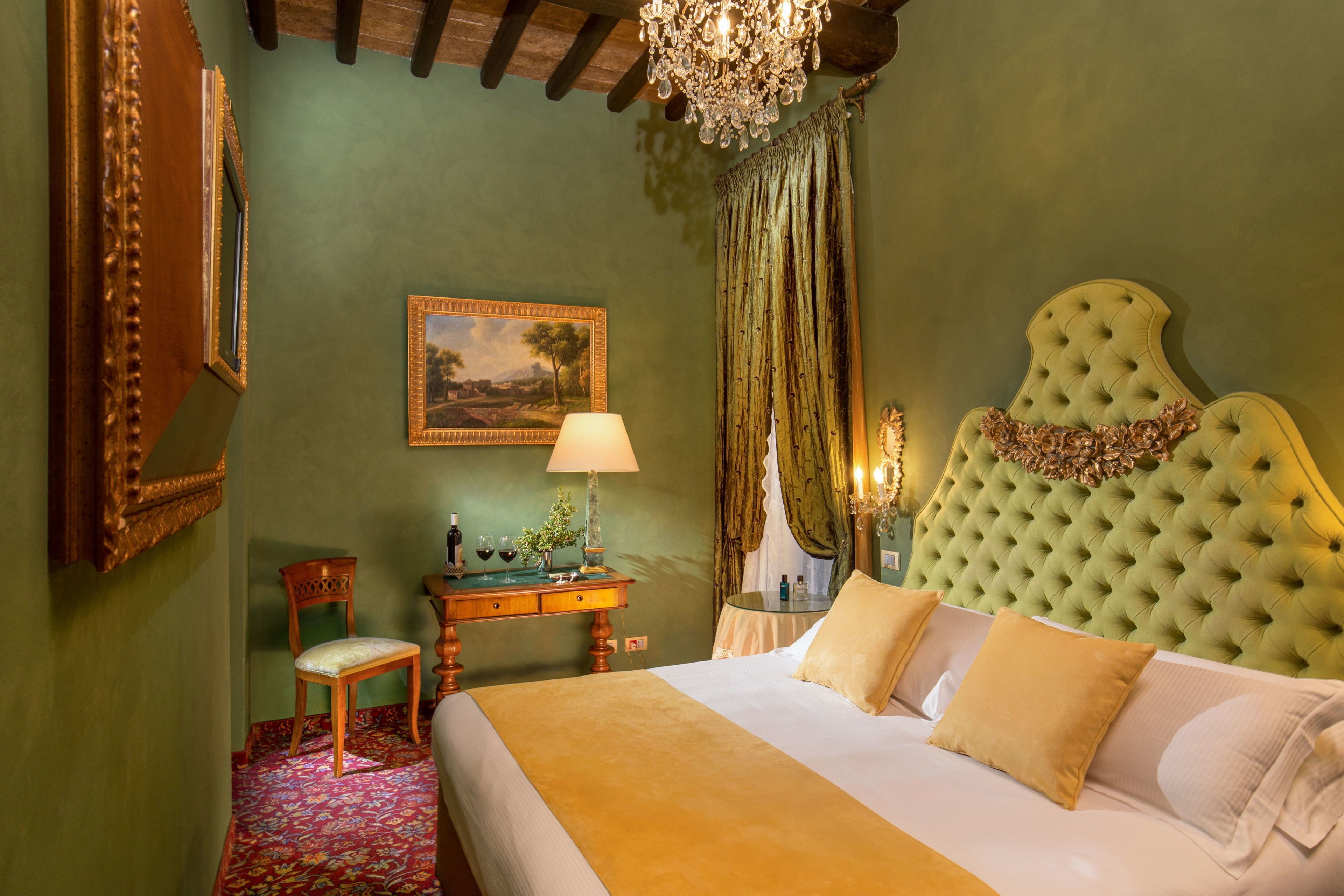 A bedroom with a large bed, a wooden chair, a desk with a lamp, and a painting on the wall.