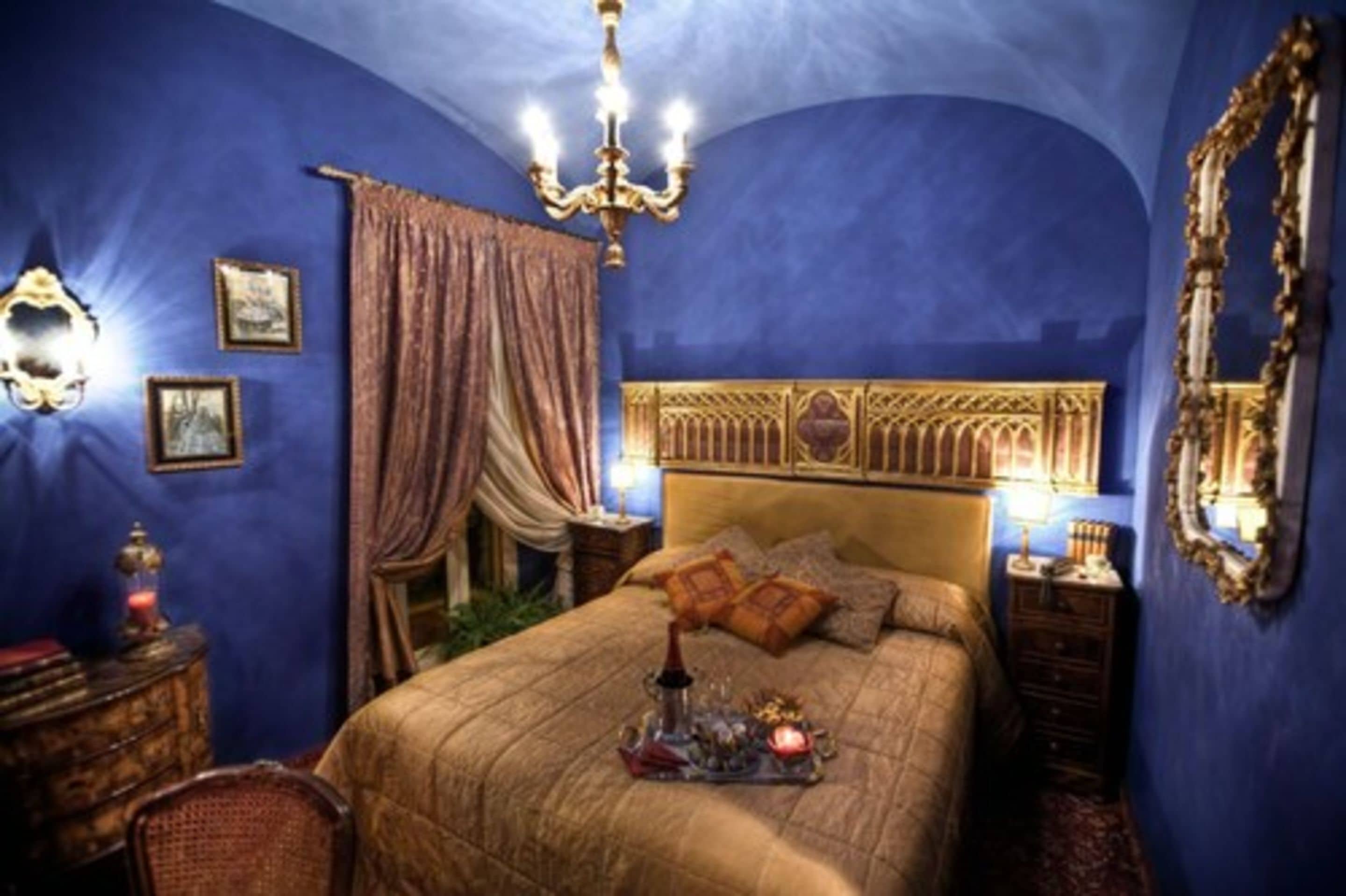 Een kamer met een groot bed, een versierd hoofdeinde en een kroonluchter.