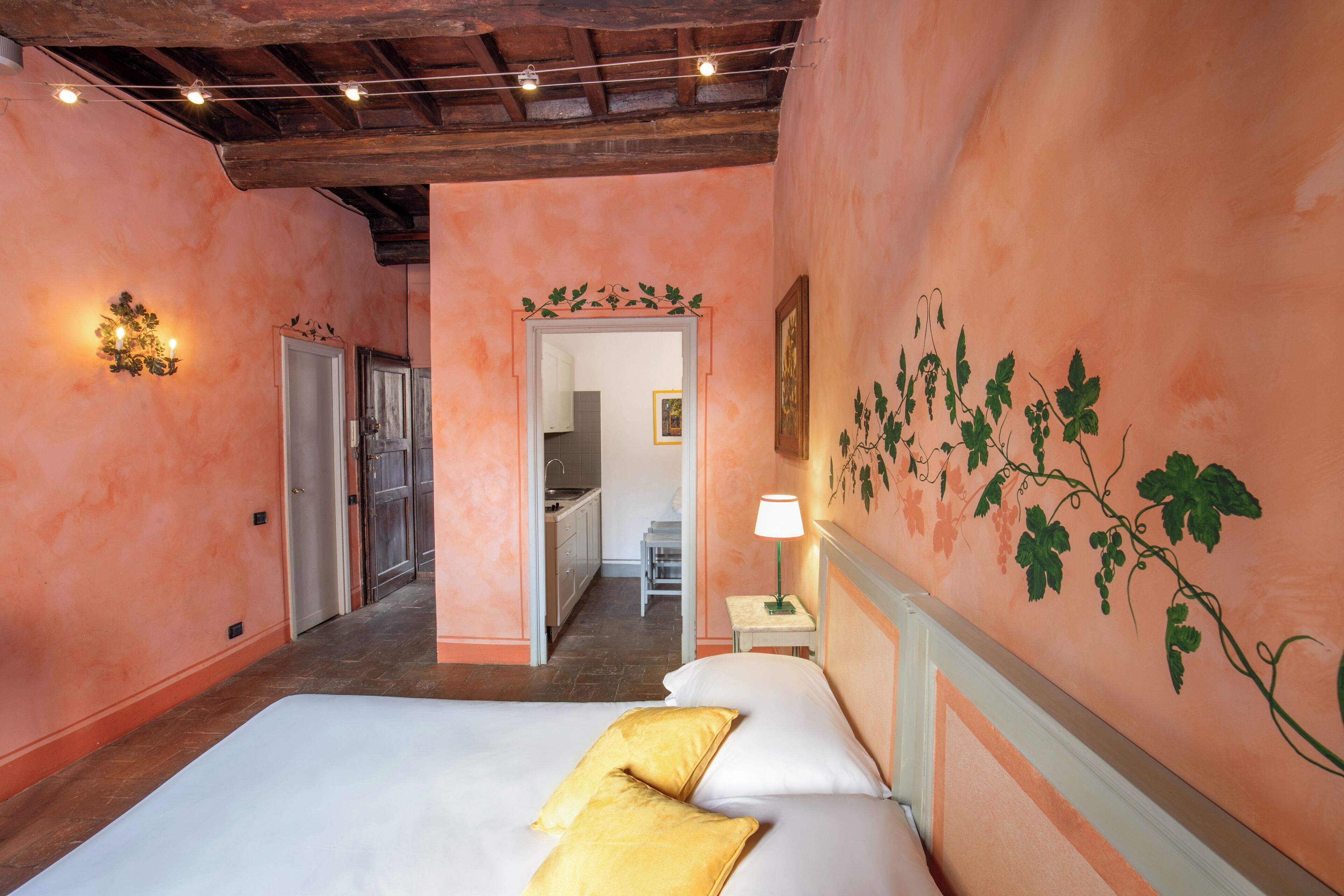 A hotel room with a bed, a nightstand, a wall-mounted lamp, and a door leading to a bathroom.