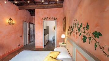 A hotel room with a bed, a nightstand, a wall-mounted lamp, and a door leading to a bathroom.