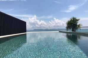 En krystalklar pool med udsigt til havet og bjergene i baggrunden.