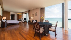 A hotel room with a large bed, a dining table with chairs, a desk with a chair, and a view of the ocean. - Villa Xilaiwan (Ratsada)
