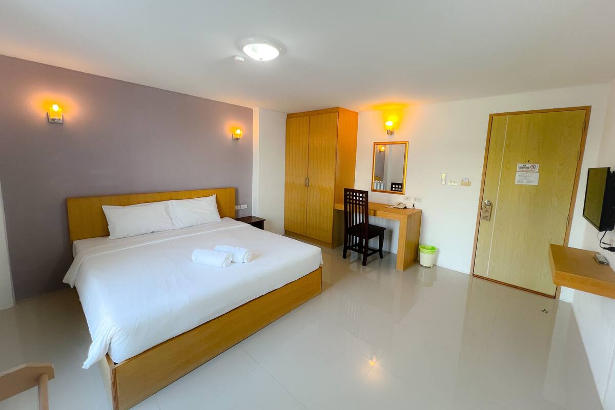 A hotel room with a bed, a desk, a chair, a wardrobe, a television, and a trash bin.