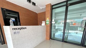 Een receptiebalie met een bordje waarop 'receptie' en '前台' in een andere taal staat, een waterdispenser en een glazen deur die naar buiten leidt.