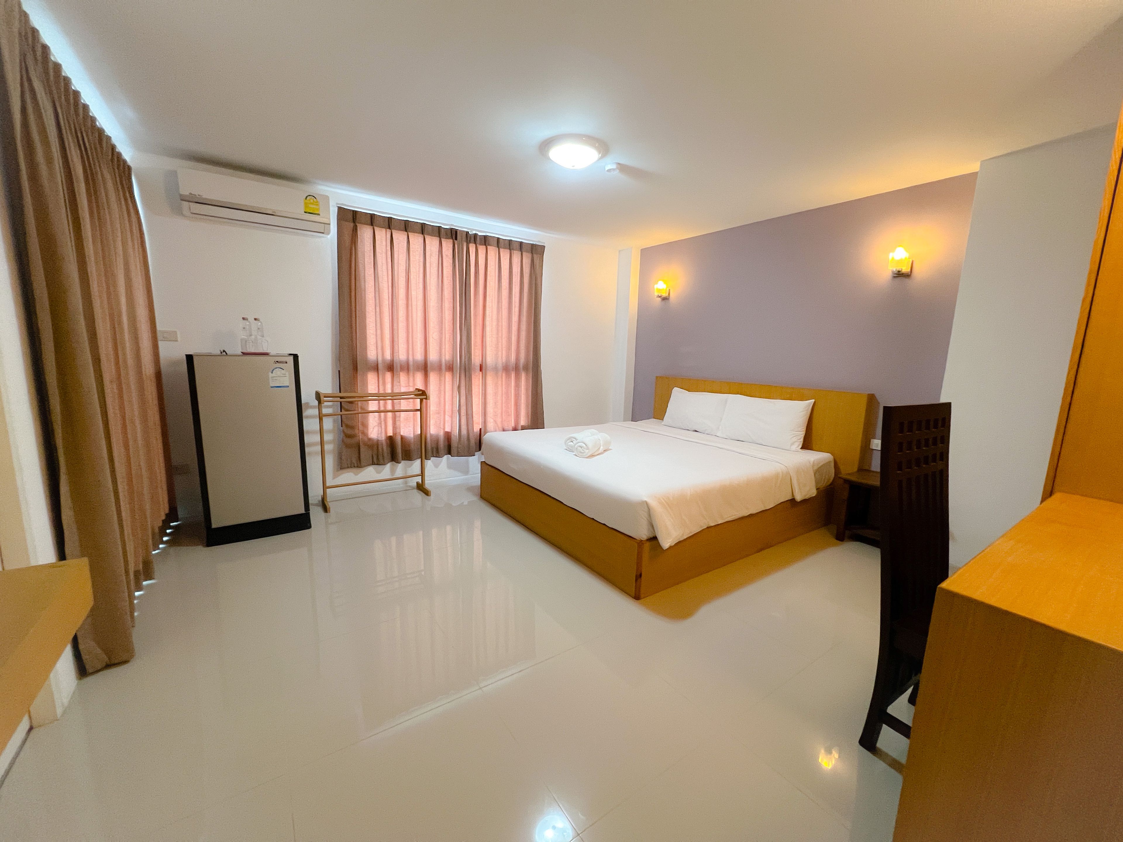 Habitación de hotel con cama, escritorio, silla, armario y ventana con cortinas.