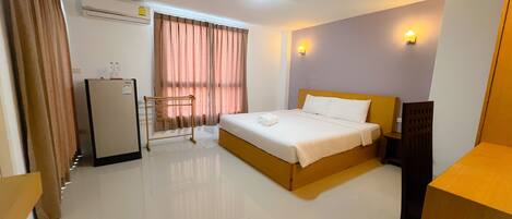 Habitación de hotel con cama, escritorio, silla, armario y ventana con cortinas.