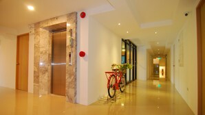 Een moderne hotelentree met een marmeren wand, een rode fiets en een gepolijste vloer.