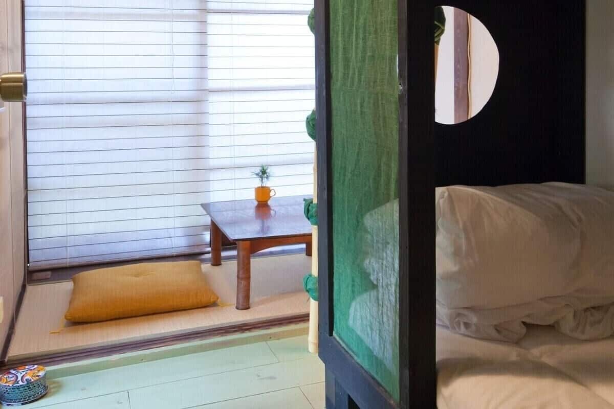 A room with a bunk bed, a small table with a plant, and a window with blinds.