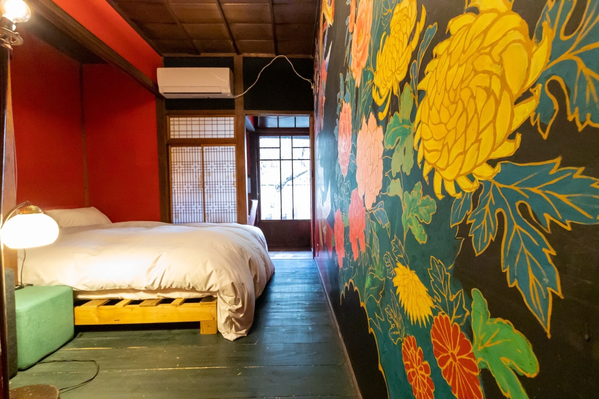 Una habitación con una cama, una silla verde, un cuadro floral en la pared y una ventana con vistas.