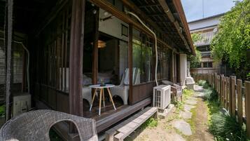 A traditional Japanese-style building with a wooden exterior, large windows, and a covered porch area with wicker furniture.