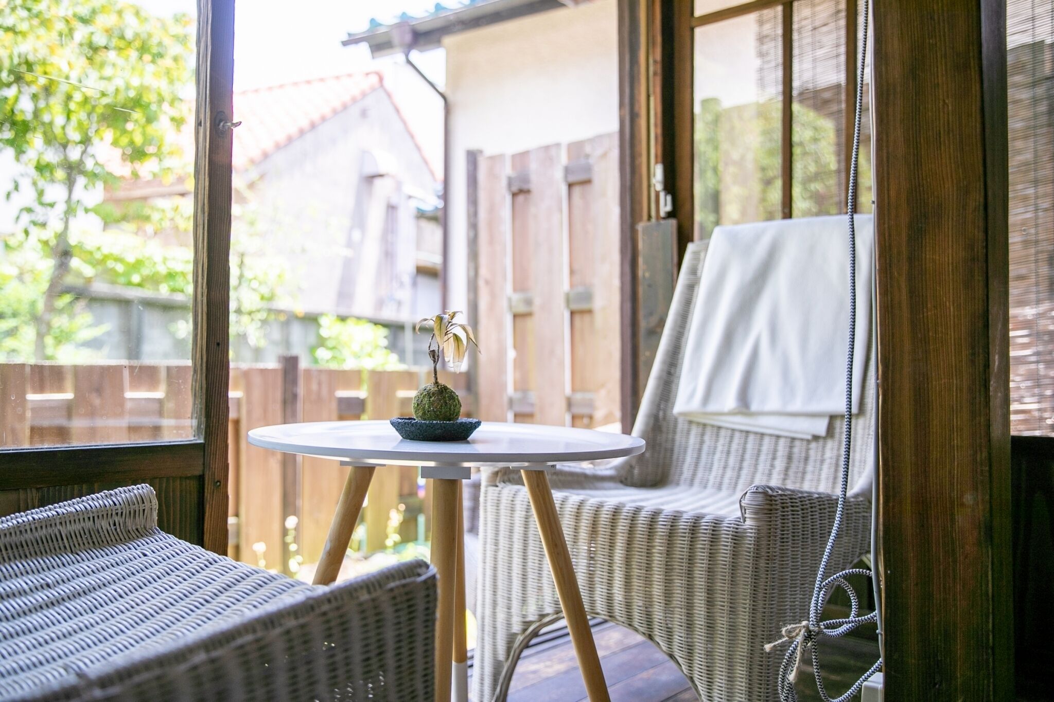 Een rieten stoel en een klein tafeltje met een plant op een balkon.