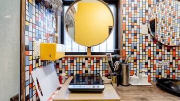 A bathroom with a colorful mosaic tile backsplash, a round mirror, a sink with a yellow soap dispenser, and a small table with a scale and a white object.