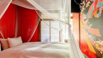 A room with a bed, red walls, a window with blinds, and a mural with a colorful design.