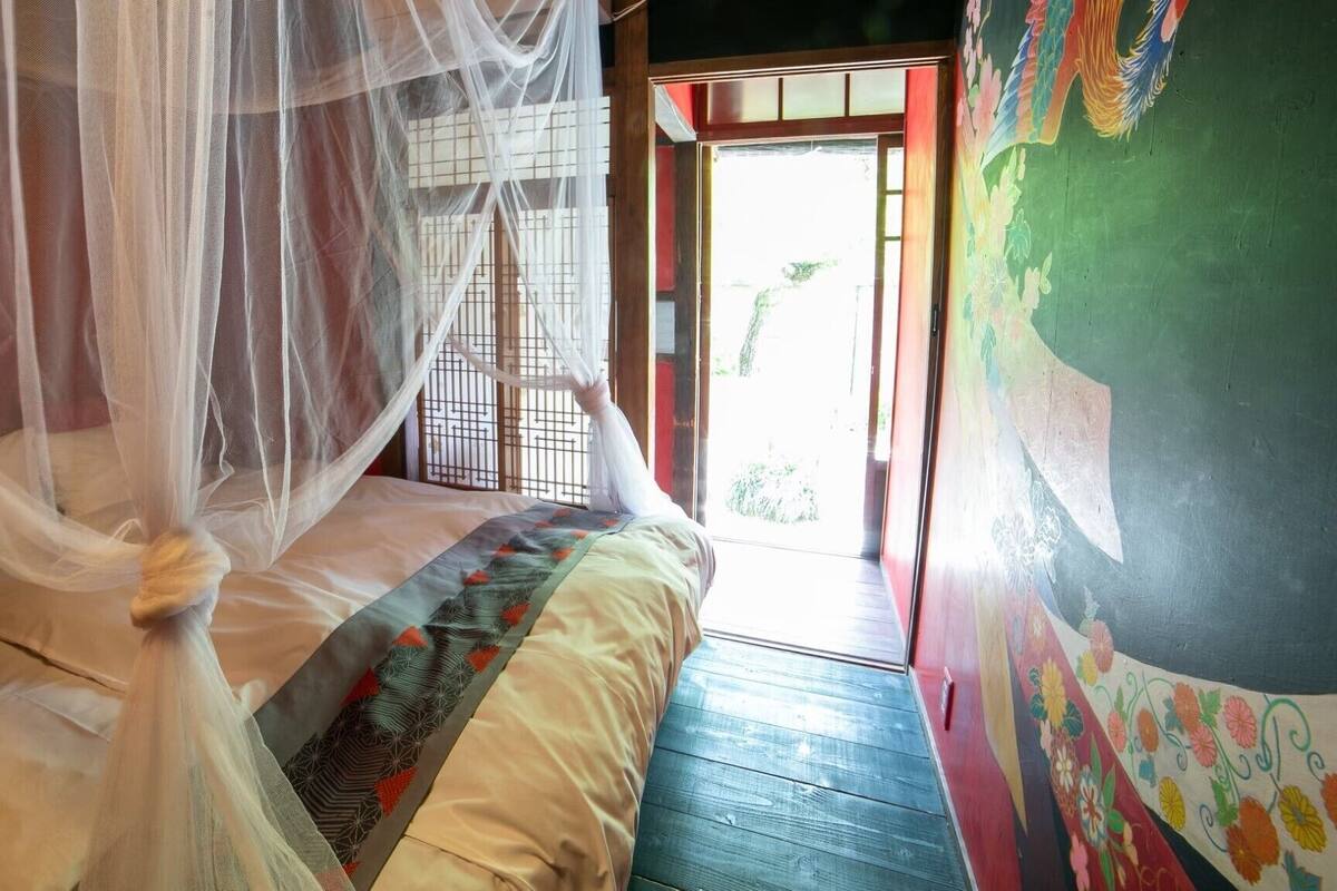 A room with a bed, a mosquito net, a wooden floor, and a door leading outside.