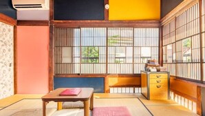 Quarto japonês tradicional com tatames, uma mesa baixa, um banco acolchoado e uma porta corrediça com barras verticais.