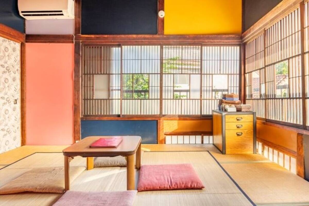 A traditional Japanese room with tatami flooring, a low table, a cushioned bench, and a sliding door with vertical bars.