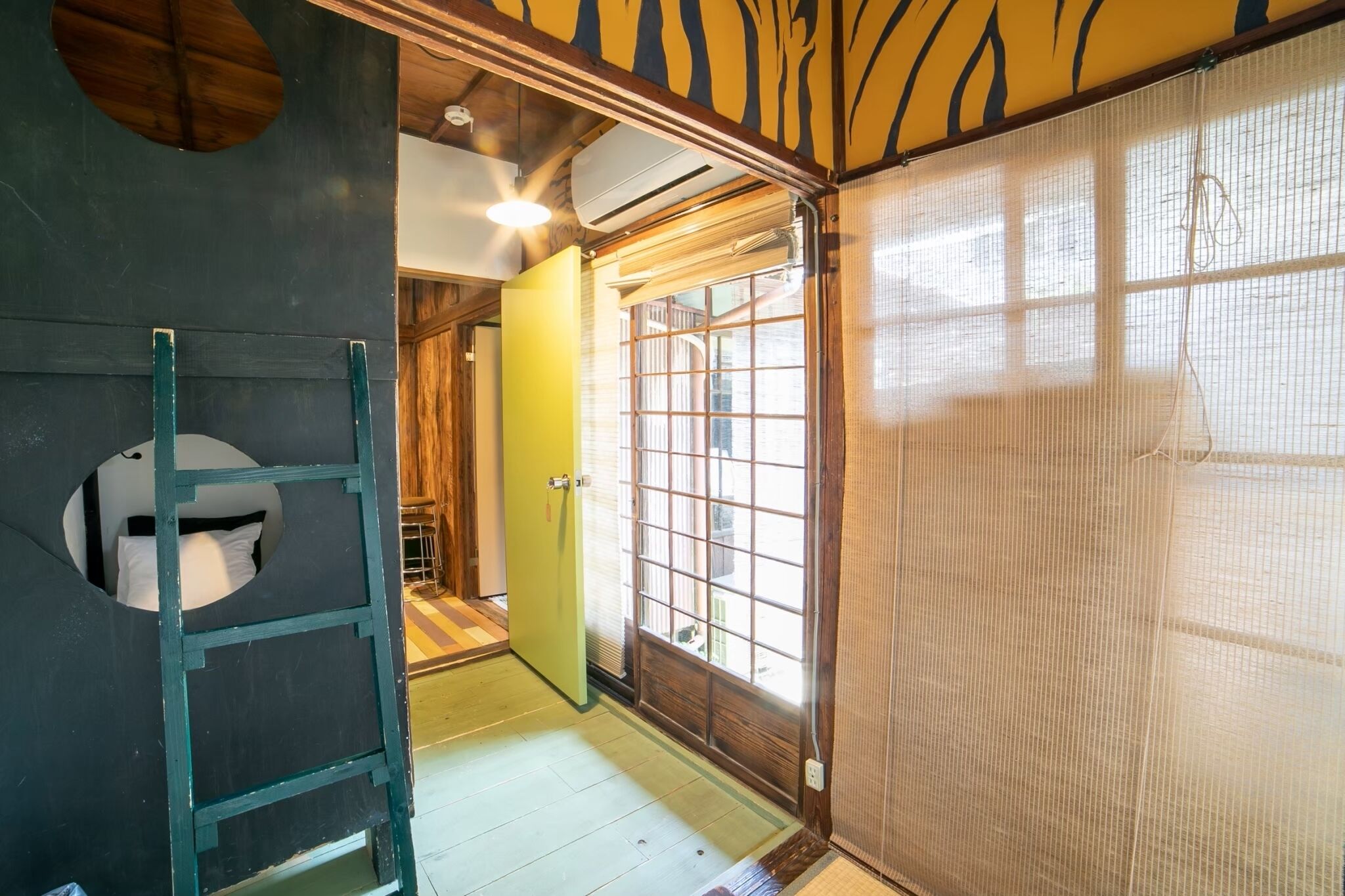 A traditional Japanese room with tatami flooring, a sliding door, and a ladder leading to a loft bed.
